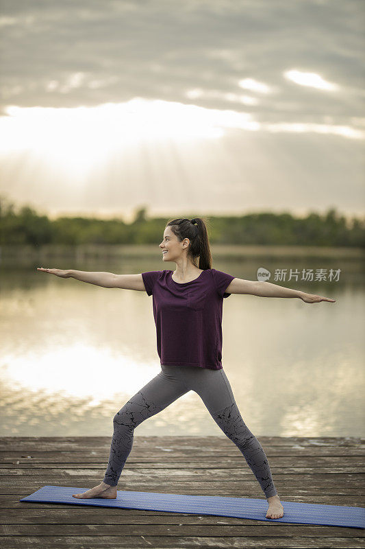 迷人的女人练习瑜伽，站在战士两个练习，Virabhadrasana II在湖码头pose